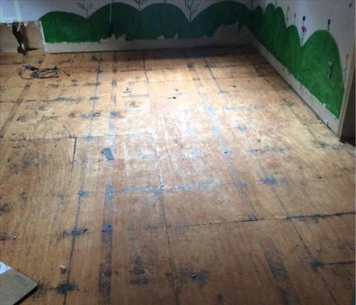 Wooden subfloor in a room with green hills painted along the wall