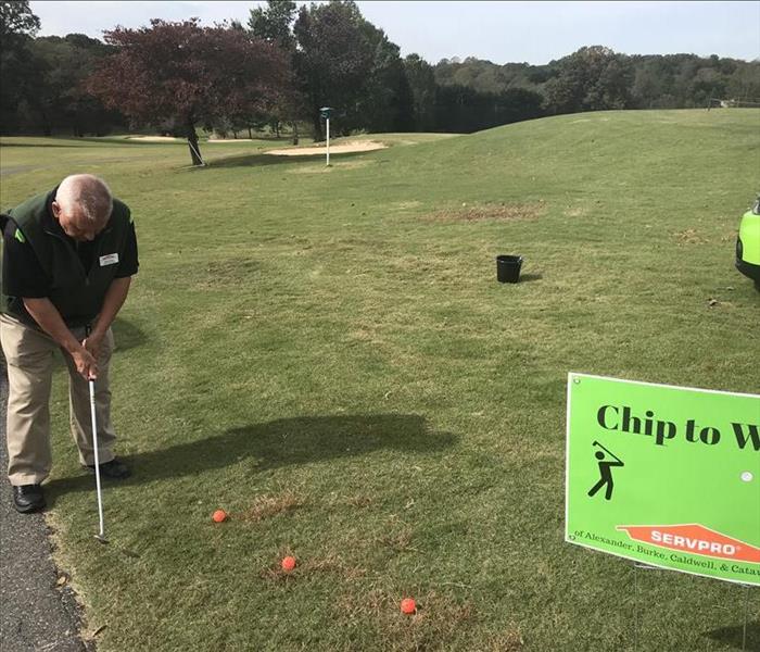Man holding a golf wedge prepares to chip orange golf balls into a black bucket on a golf course