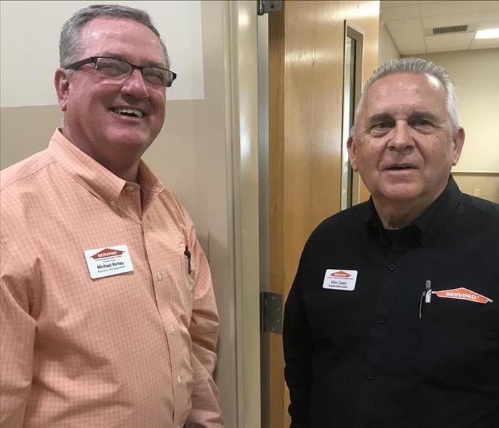 Two SERVPRO employees standing side-by-side in front of an open entryway
