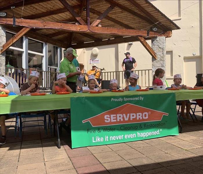 Children wearing paper hats sit at light-green table with SERVPRO banner on the front