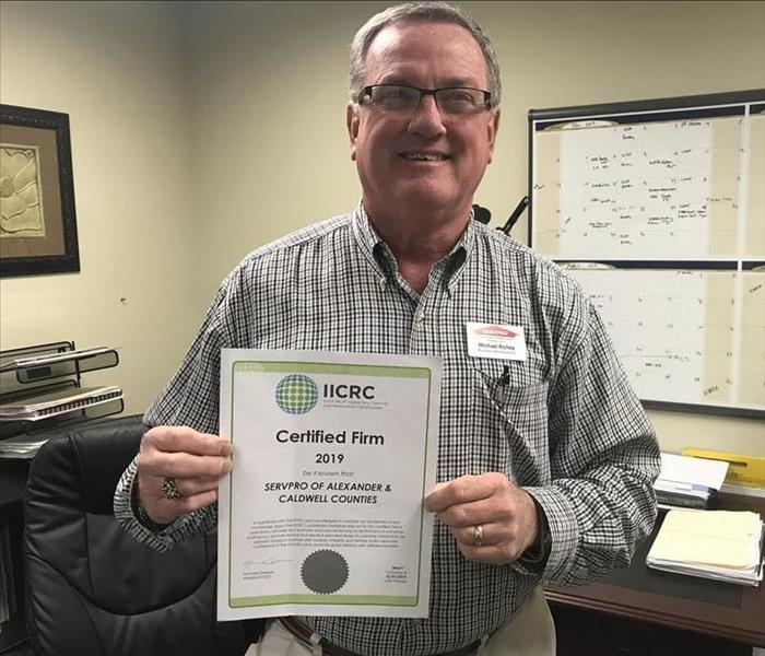 Man with SERVPRO badge holding a document that says "Certified Firm"