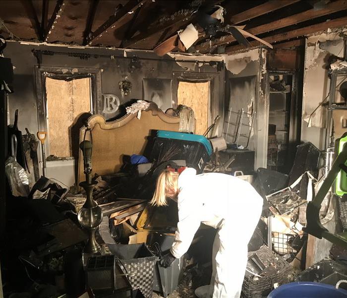Woman in white PPE lifting object in a fire-damaged room