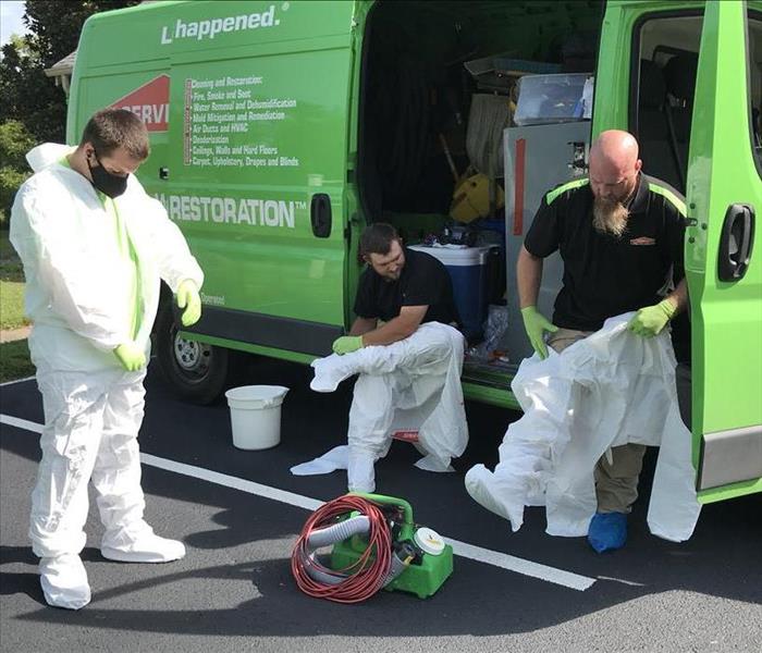 Three male SERVPRO employees putting on white PPE in front of a green SERVPRO van