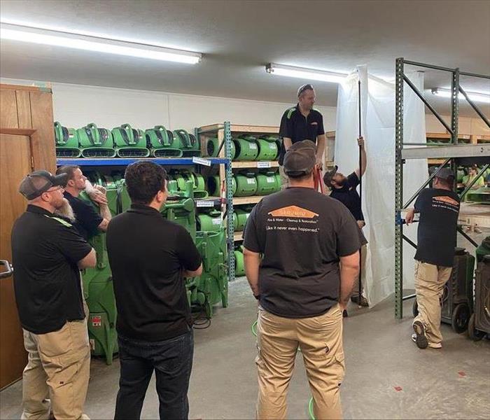 SERVPRO employees standing around and watching a man put up plastic sheet