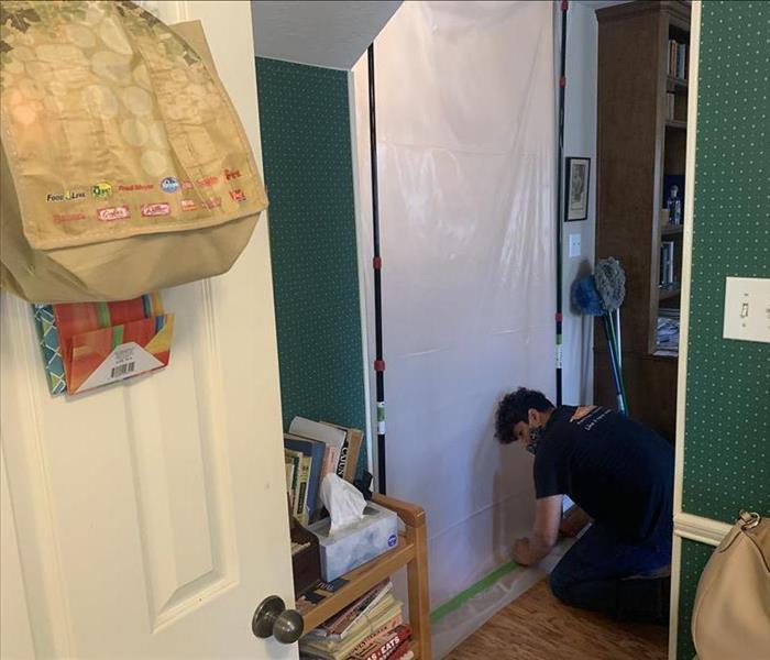 Crouched SERVPRO employee placing plastic cover over door opening