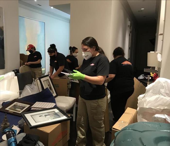 Women wearing SERVPRO uniforms and masks boxing items in a room