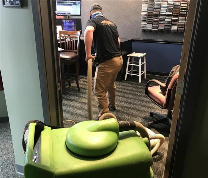 SERVPRO employee extracting water from carpet with green, vacuum-like machine