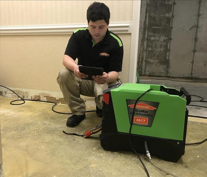 Male SERVPRO employee crouched next to green machine looking at a tablet