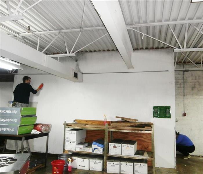 Person on step ladder wiping a white wall in a commercial space