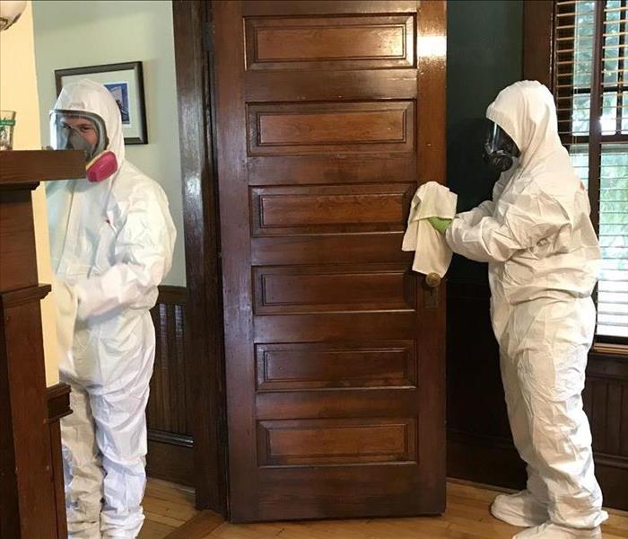 Two people in white PPE wiping down surfaces in a room