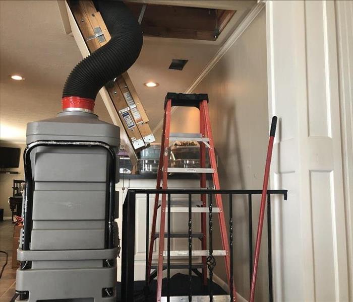 Black tube of gray vacuum enters attic above cluttered room