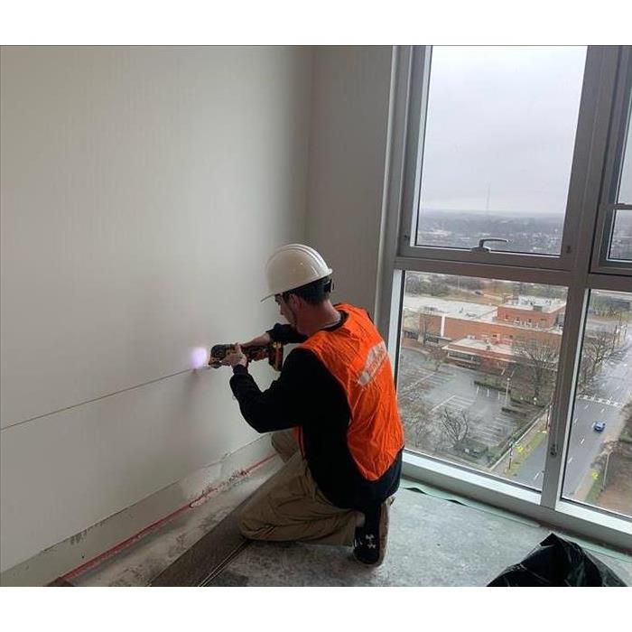 A SERVPRO employee cuts out a section of drywall so he can dry hidden moisture in this water-damaged building.