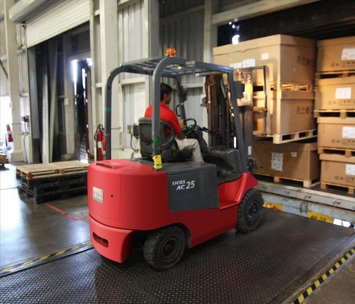 A person wearing a red shirt operates a red forklift at a warehouse